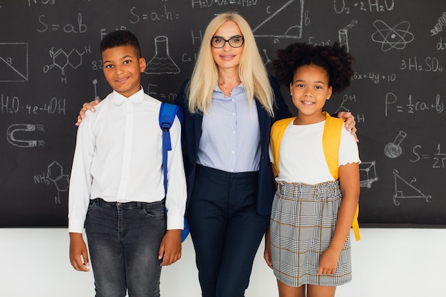 L'insegnante femminile felice abbraccia i bambini delle scuole vicino alla lavagna squadra internazionale ritorno a scuola