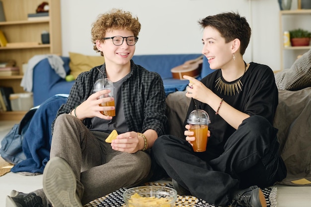 Happy female teenager with glass of juice or soda looking at her boyfriend