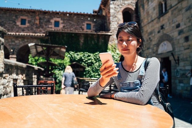 happy female tour guide sitting outdoor in the old medieval castle waiting for her group finish sightseeing visit the ancient building in europe. girl using mobile phone chatting with friends online.