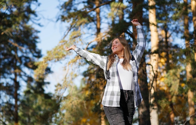 happy female tourist goes camping through the forest raising her hands and smiling