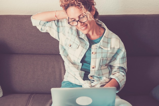 Happy female use laptop online computer at home sitting on the sofa smiling and having fun  modern