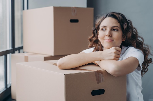 Happy female with cardboard boxes resting during packing things\
dreaming about new home moving day