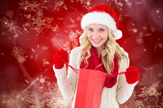 Happy festive blonde with shopping bag against red snow flake pattern design