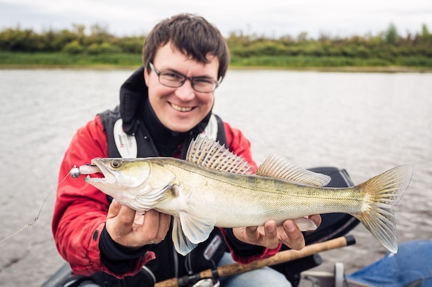 Happy fisher with pike perch looking at camera