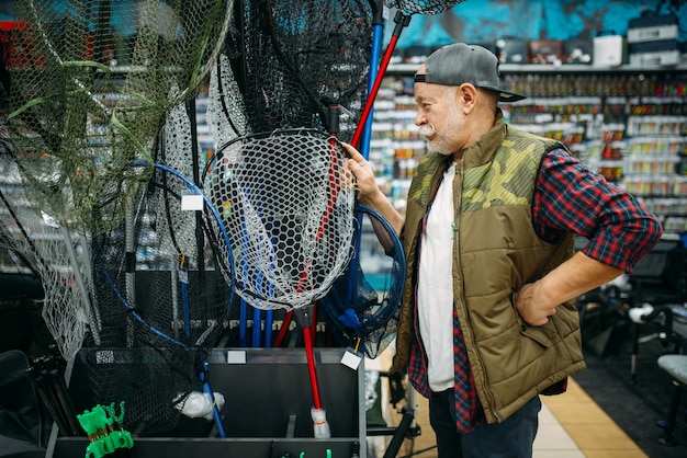 Happy fisherman choosing net in fishing shop, hooks and baubles