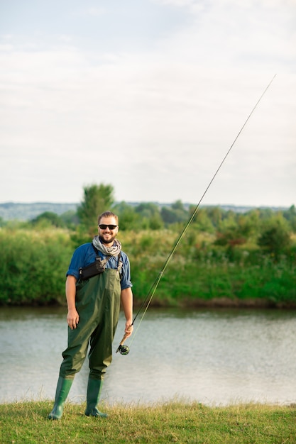 Pescatore felice con il vestito speciale e la canna da pesca vicino al fiume