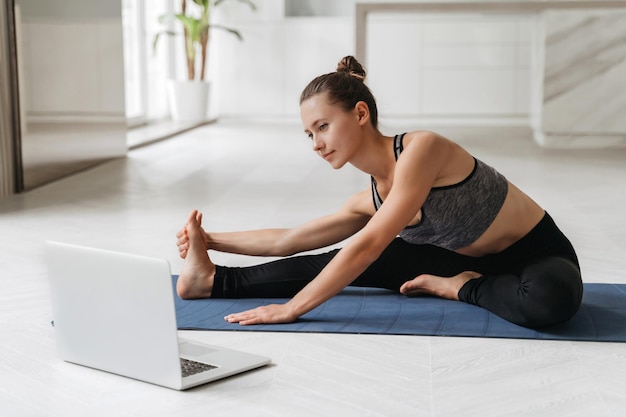 Happy fit female practicing yoga at home with laptop