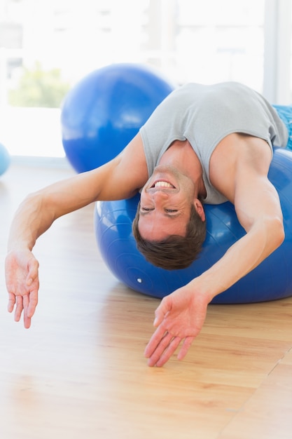 Uomo felice di misura che allunga sulla palla di esercizio in palestra