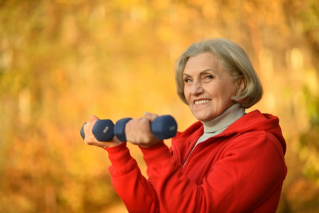 Happy fit senior vrouw trainen in herfst park dumbbells