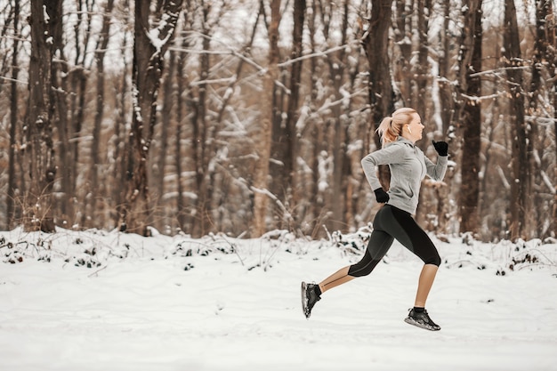 Happy fit sportswoman jogging in nature at snowy winter day. Healthy life, winter sport