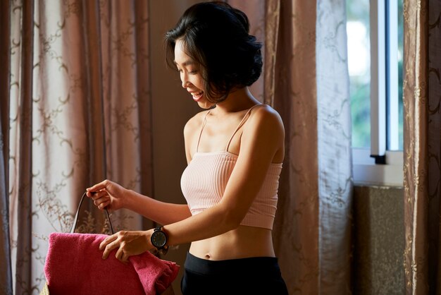 Happy fit young woman putting soft towel in bag when going to fitnes training