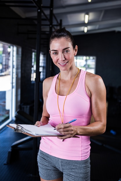 Happy fitness instructor holding clipboard in gym