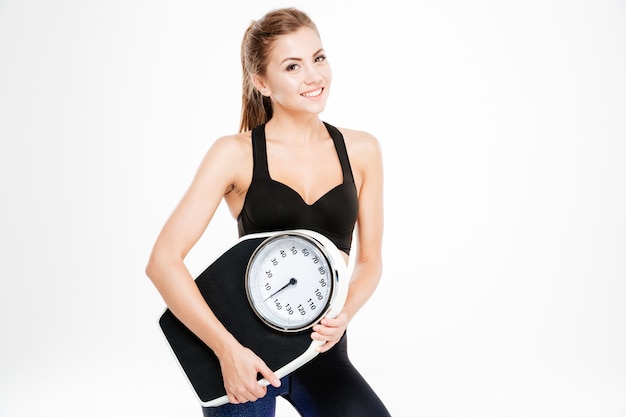 Happy fitness woman holding weighing machine isolated