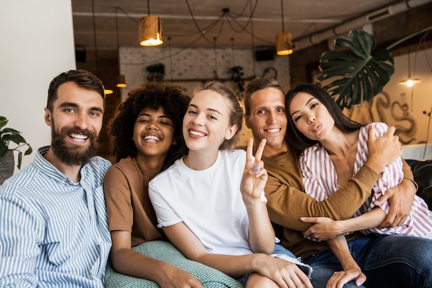 Happy five friends in a cafe shop smiling at the camera making a group photo