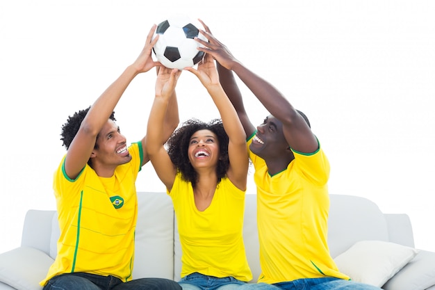 Счастливый футбольных болельщиков в желтый, сидя на диване с мячом