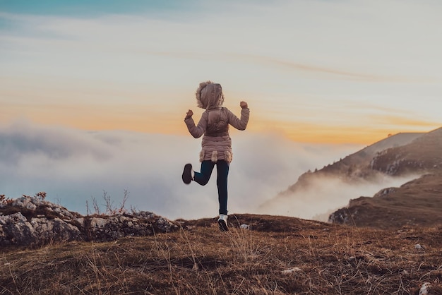 A happy free girl joyfully jumps on the top mountain at sunset