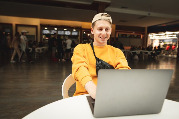 Happy freelancer sits at the table in a food court at a shopping mall