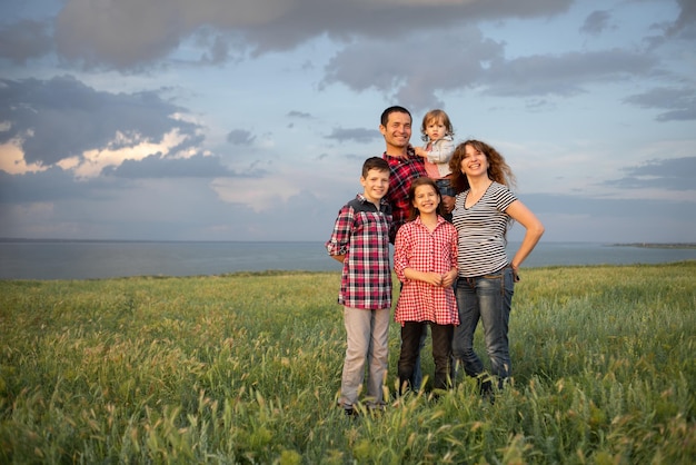 Happy friendly big family with three children two sons and a daughter stand in the summer at sunset background of the cloudy blue sky in the evening