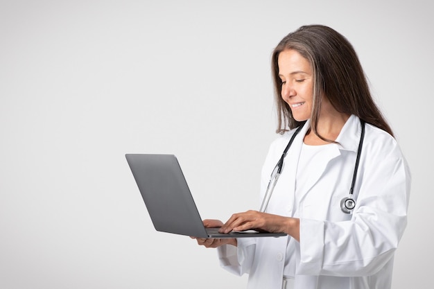 Happy friendly caucasian senior therapist woman in white coat typing on computer chatting with