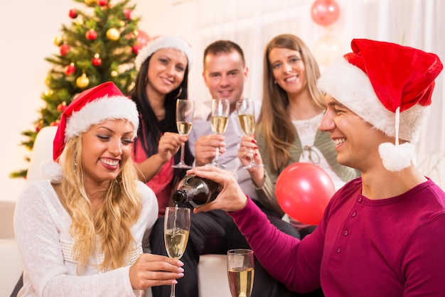 Happy friends Celebrating Christmas or New Year with glass of champagne in home interior.