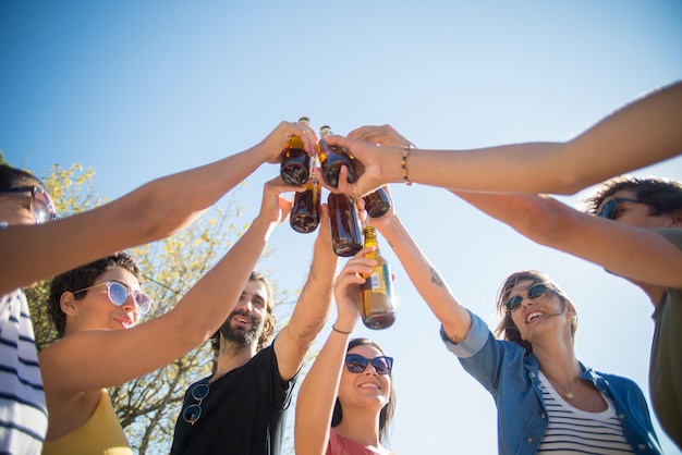 週末を祝うビール瓶をチリンと鳴らす幸せな友達。さまざまな国籍の人々がボトルを上げて笑っています。パーティー、友情の概念