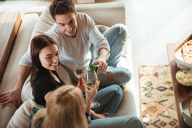 Happy friends clinking giving toasts and clinking glasses on sofa