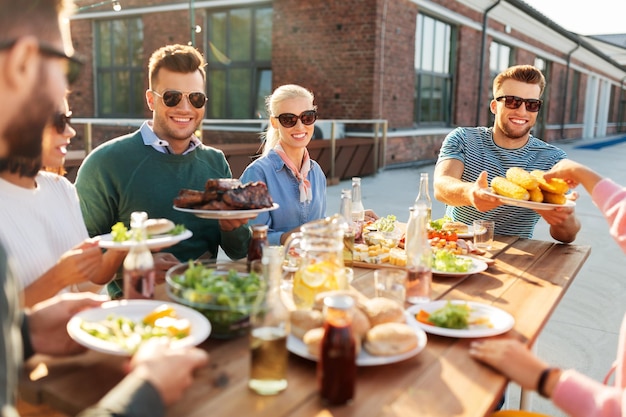 happy friends eating at barbecue party on rooftop