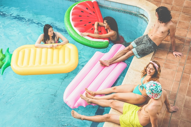 Happy friends floating with air lilo ball at swimming pool party - Young people having fun on summer holidays vacation