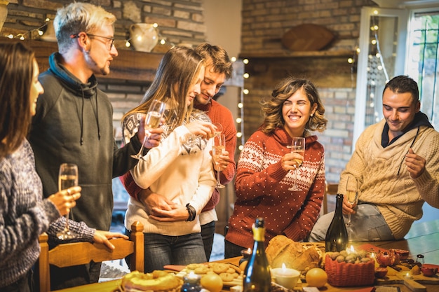 Группа счастливых друзей празднует рождественскую вечеринку с белым вином и сладкими блюдами за ужином