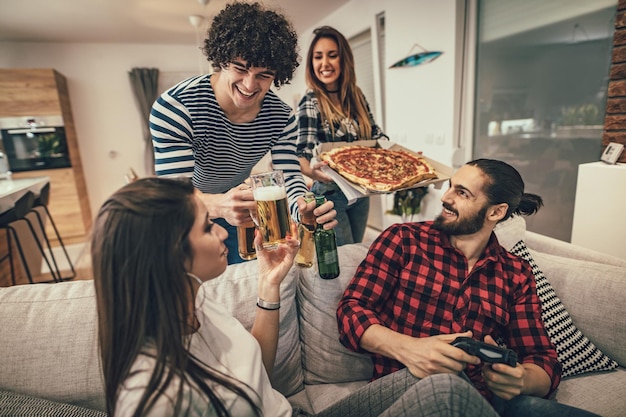 Foto amici felici che si divertono mentre mangiano pizza e bevono birra. hanno un ottimo fine settimana in bella compagnia al chiuso.