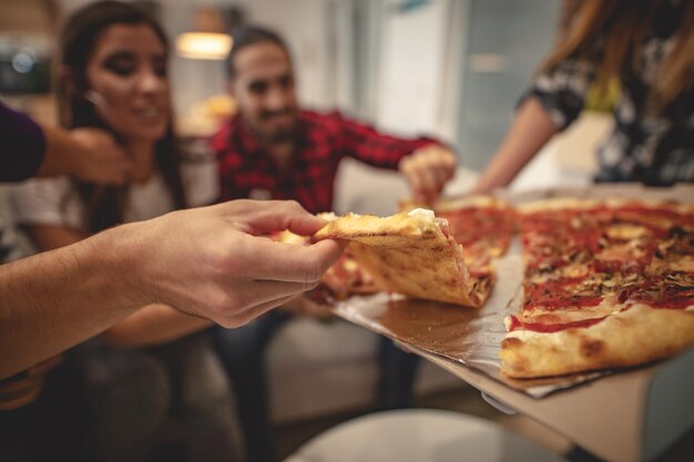 ピザを食べながら楽しんでいる幸せな友達。彼らは屋内で素敵な会社で素晴らしい週末を過ごします。