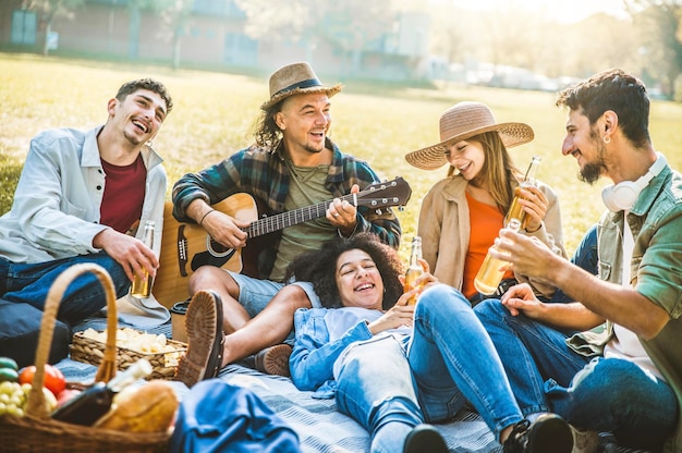 Amici felici che fanno picnic nel parco gruppo di giovani che si divertono insieme cantando e suonando