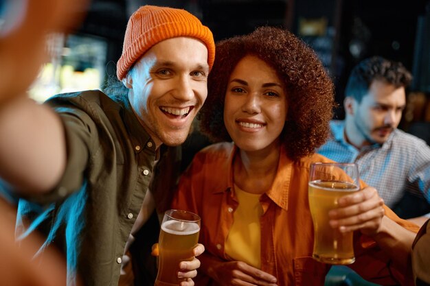 Happy friends holding beer glasses taking selfie photo for memory while rest at sports bar