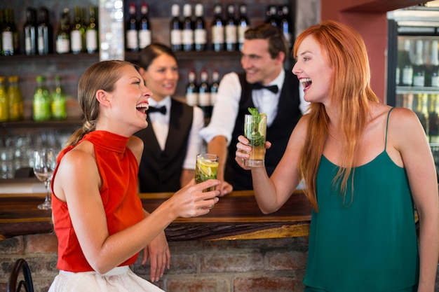 Счастливые друзья держат стакан джина перед барной стойкой