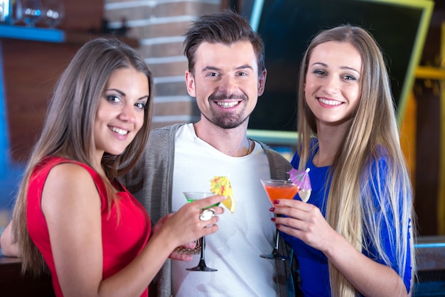 Happy friends holding glasses with cocktails in bar.