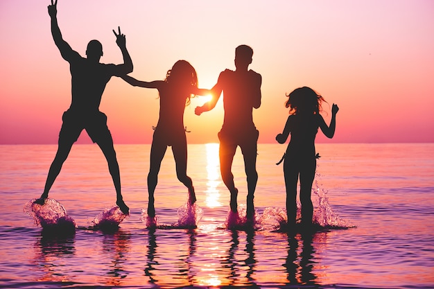 Happy friends jumping inside water on tropical beach at sunset