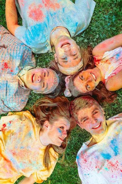 Happy friends laying on green grass ground dirty in holi paints indian holiday