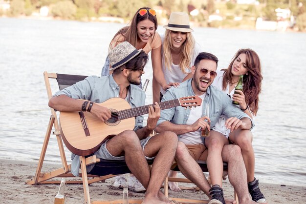 Happy friends playing guitar on the beach