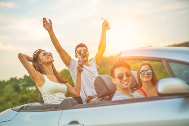 The happy friends sit in a cabrio on the sunny background