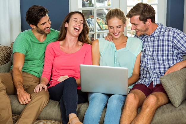 Happy friends sitting on sofa and using laptop