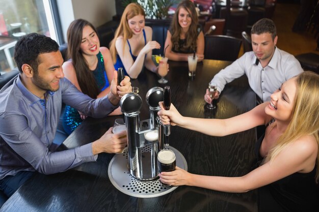 Happy friends sitting together and pulling pints