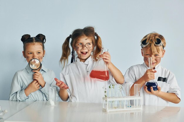 Photo happy friends smiling children in white coats plays a scientists in lab by using equipment