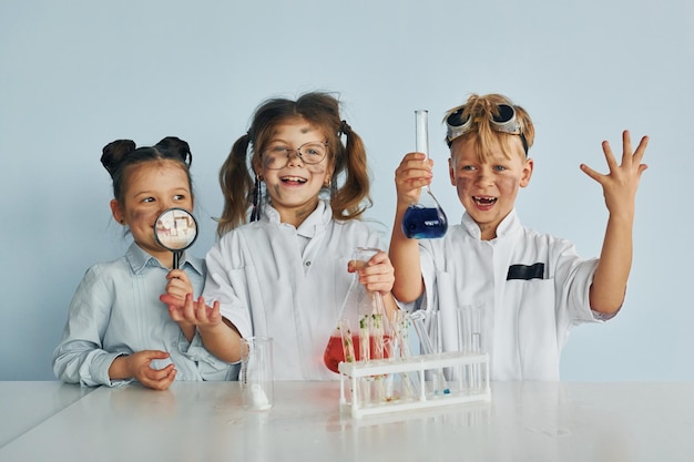 웃는 행복한 친구들 흰 가운을 입은 아이들이 장비를 사용하여 실험실에서 과학자를 연기합니다