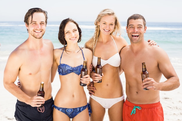 Happy friends standing on the beach with beer bottles