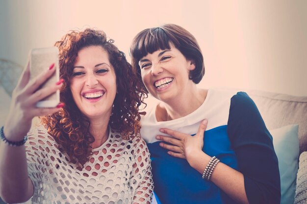 Happy friends taking selfie while sitting against wall