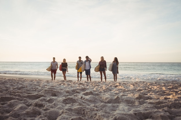 Foto amici felici che camminano con tavole da surf