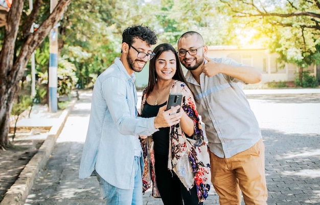 Amici felici che guardano un cellulare per strada tre amici felici che condividono il cellulare per strada concetto di amici felici che condividono contenuti multimediali su un telefono