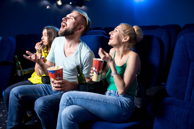 Happy friends watching film sitting together with popcorn in the cinema