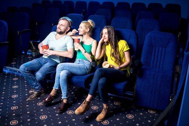 Счастливые друзья смотрят фильм, сидя вместе с попкорном в кинотеатре