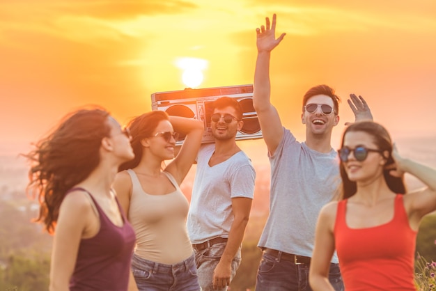 The happy friends with a boom box dancing on the bright sun background